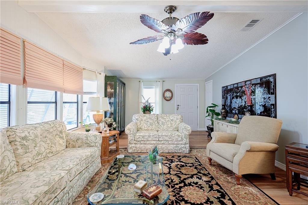 Living area with a textured ceiling, wood finished floors, ceiling fan, crown molding, and lofted ceiling
