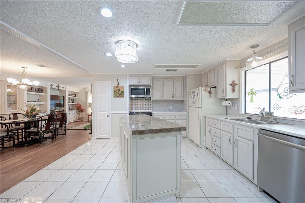 Kitchen featuring appliances with stainless steel finishes, a sink, a center island, decorative backsplash, and light tile patterned floors