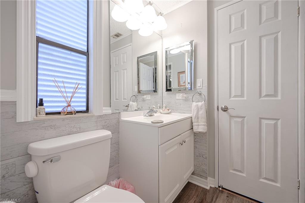 Bathroom featuring toilet, vanity, tile walls, ornamental molding, and a chandelier with tub/shower
