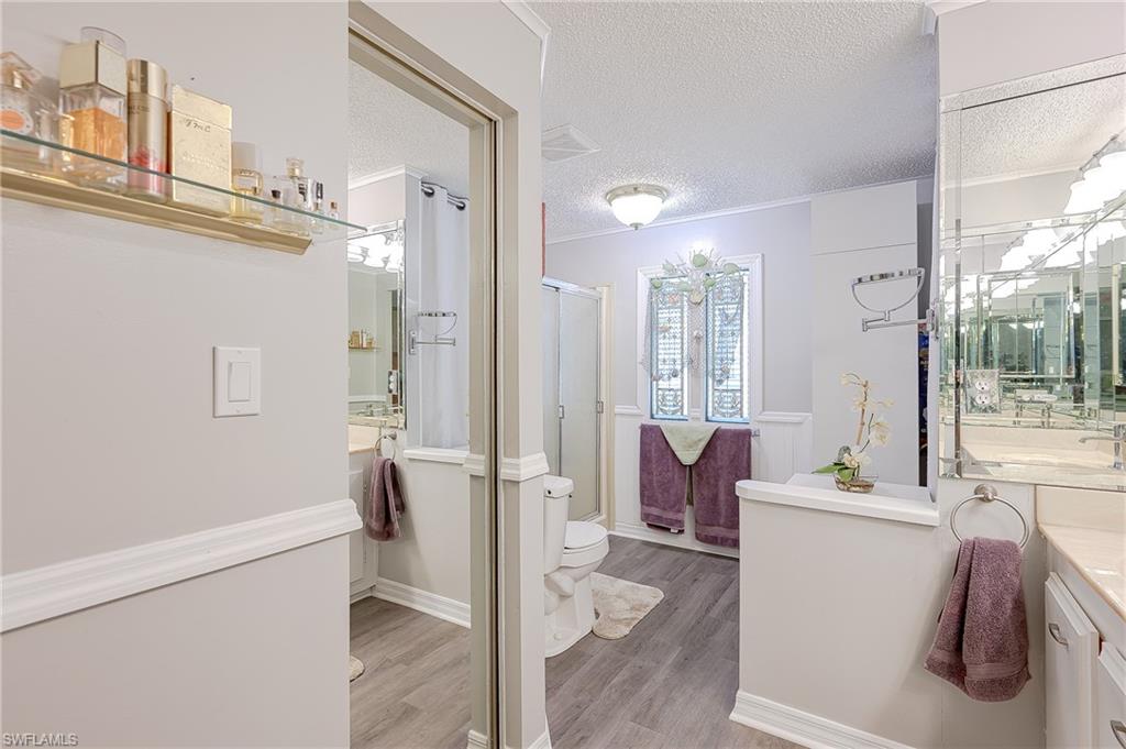 Full bath featuring a textured ceiling, wood finished floors, vanity, toilet, and a stall shower