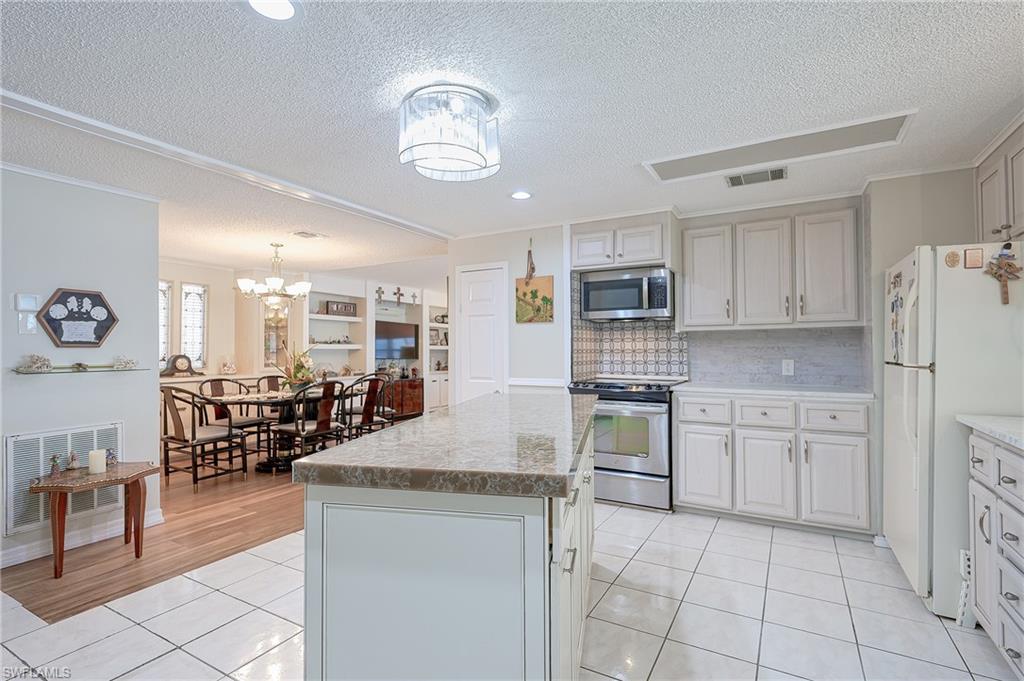Kitchen with appliances with stainless steel finishes, a textured ceiling, a chandelier, light tile patterned floors, and a center island