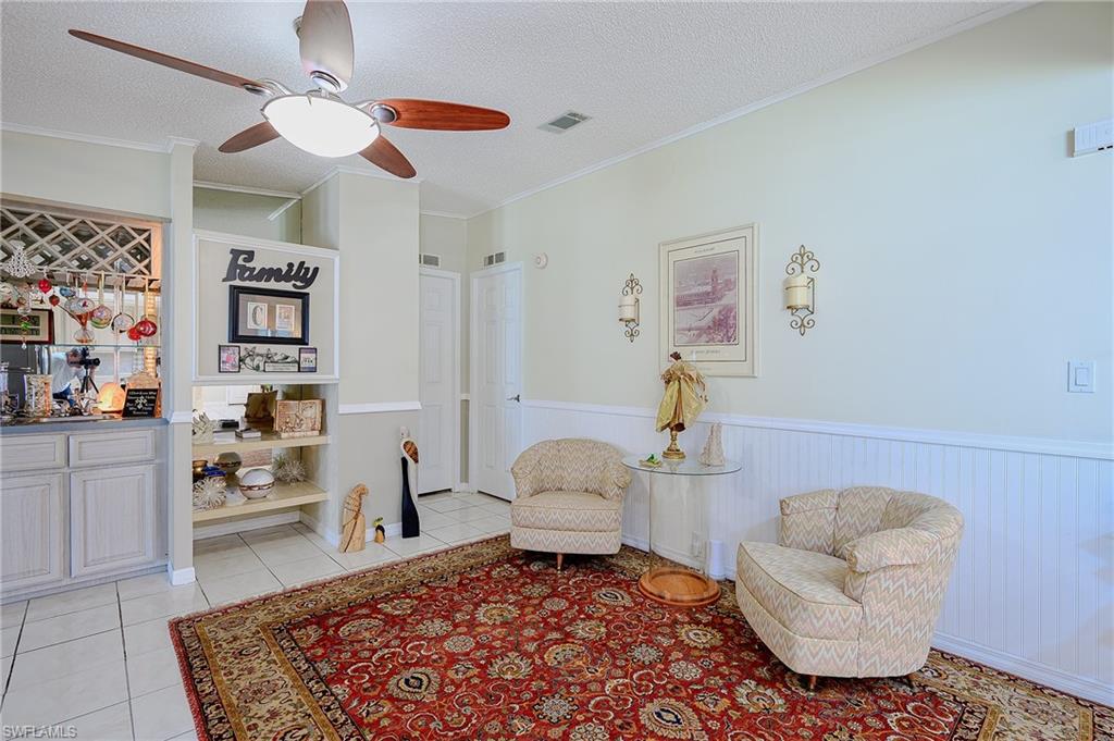 Sitting room featuring wainscoting, a textured ceiling, ceiling fan, light tile patterned flooring, and crown molding