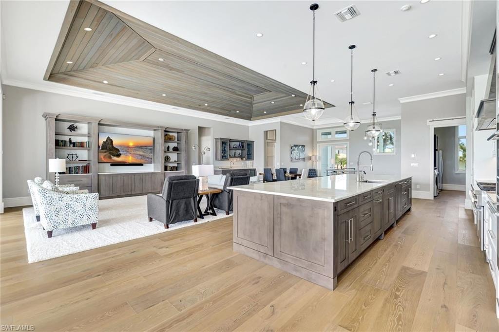 Kitchen featuring a sink, ornamental molding, light wood-style flooring, a large island, and stainless steel refrigerator