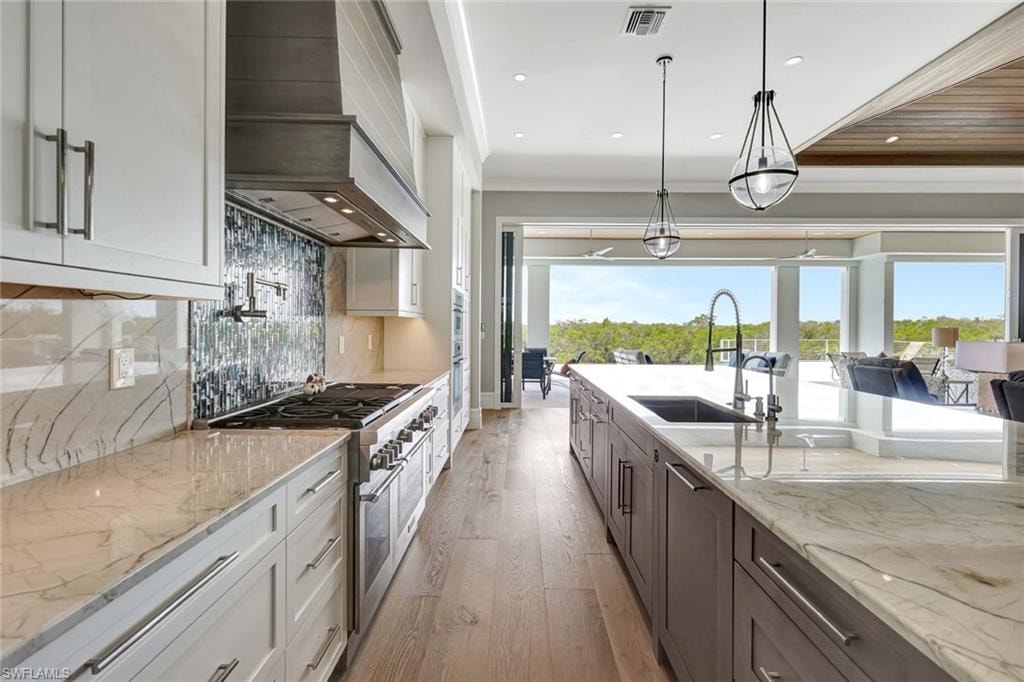 Kitchen with custom range hood, range with two ovens, light wood-style floors, white cabinetry, and recessed lighting