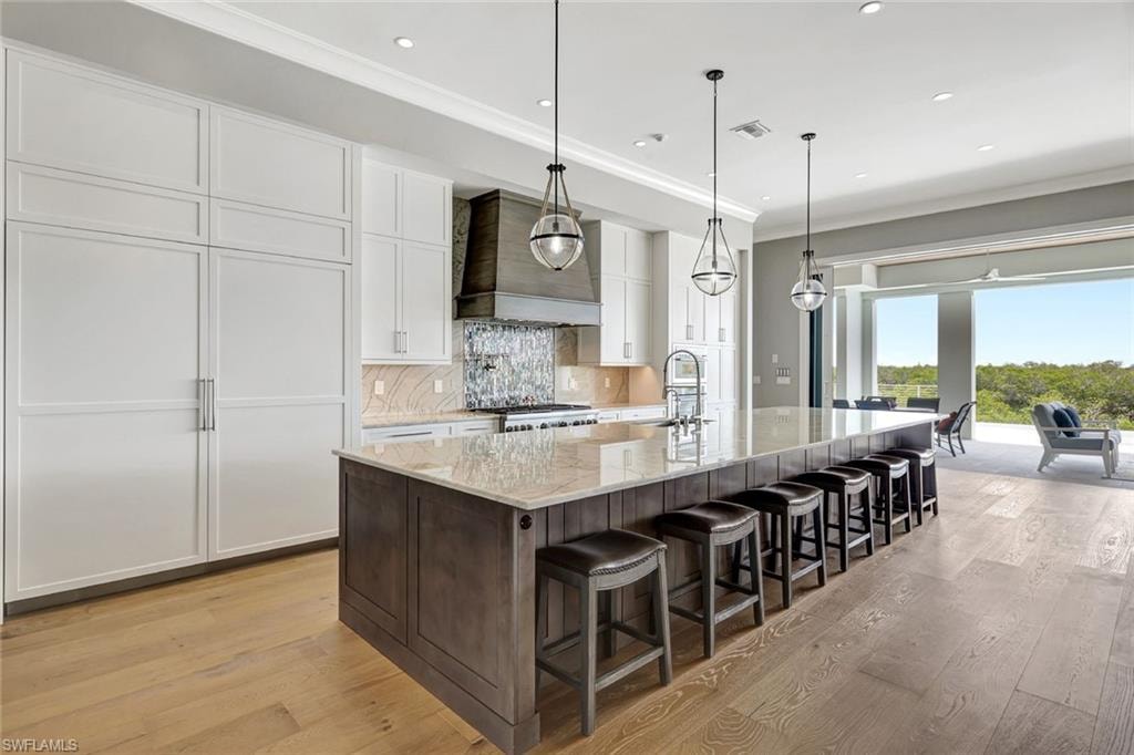 Kitchen with premium range hood, a sink, white cabinets, light wood-style flooring, and crown molding