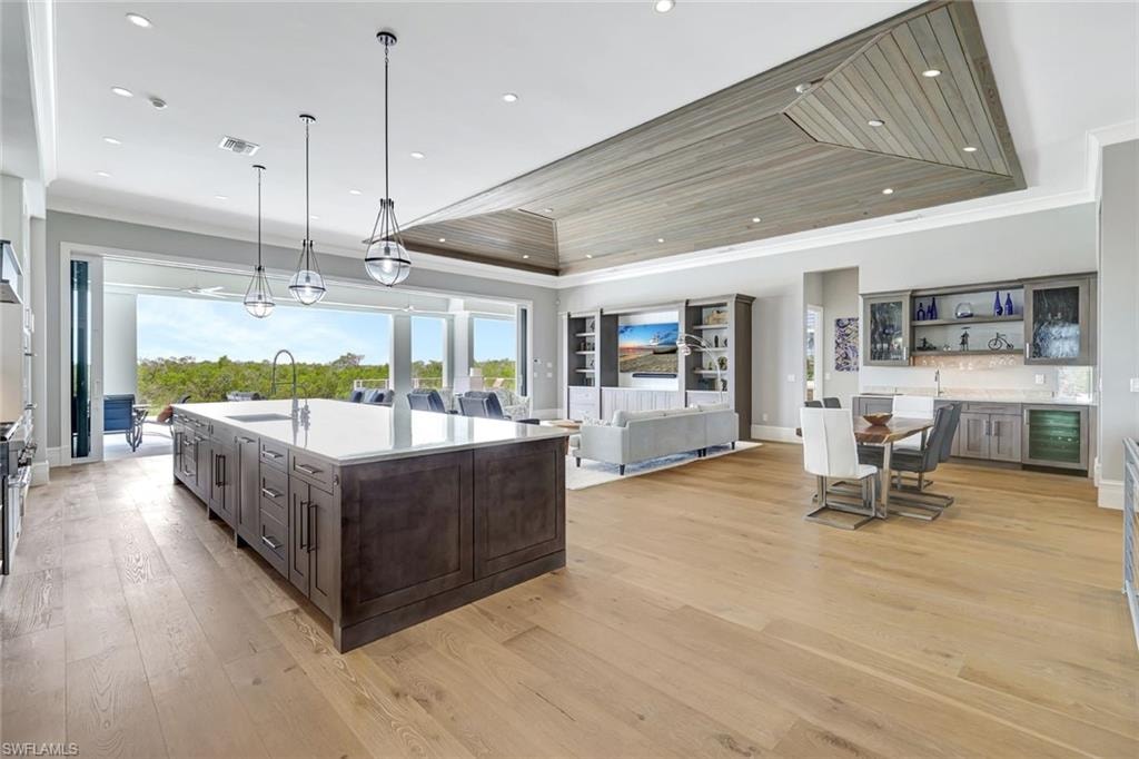 Kitchen featuring wine cooler, a raised ceiling, a sink, dark brown cabinets, and light countertops