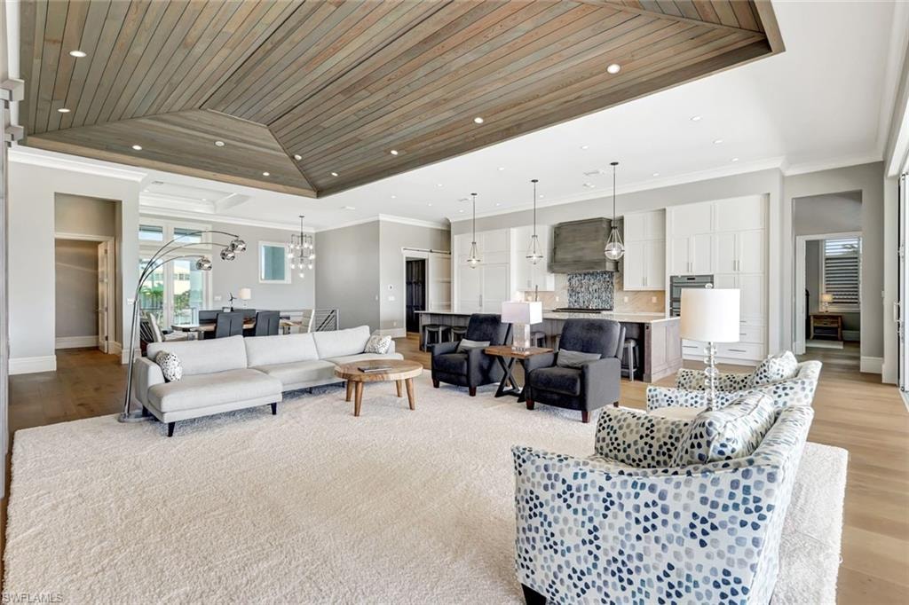 Living area featuring light wood-style flooring, baseboards, a tray ceiling, crown molding, and wooden ceiling