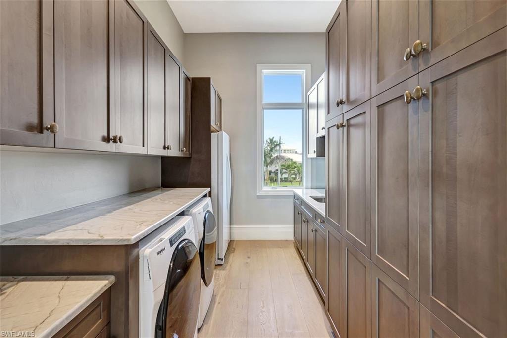 Laundry room featuring washer and clothes dryer, baseboards, light wood-type flooring, and cabinet space