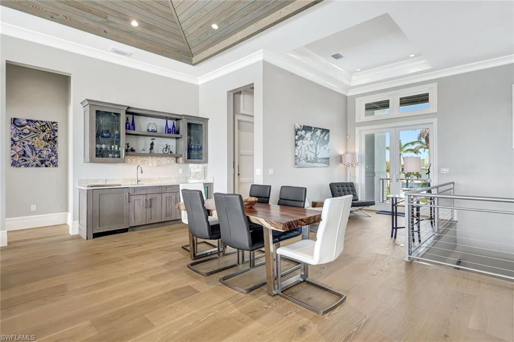 Dining room featuring bar with sink, a raised ceiling, light wood-type flooring, french doors, and recessed lighting