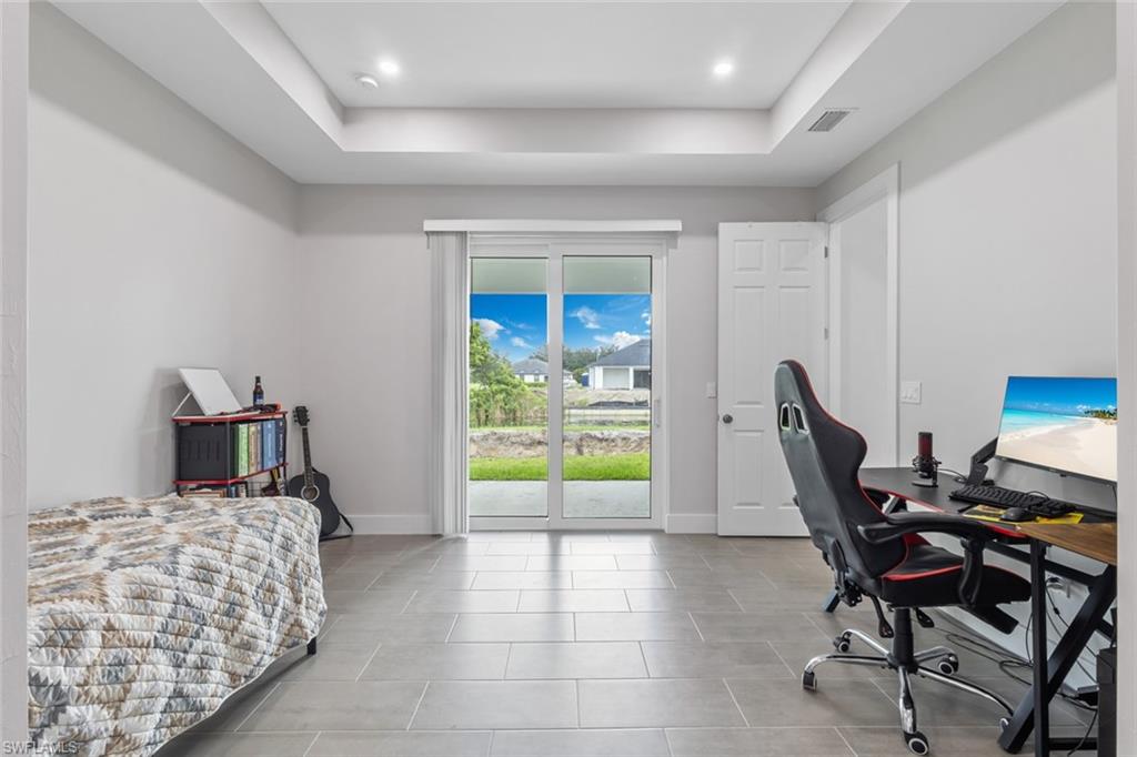 Tiled bedroom with a tray ceiling, access to outside, and a desk