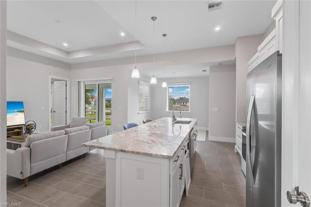Kitchen with freestanding refrigerator, open floor plan, white cabinetry, an island with sink, and light stone counters