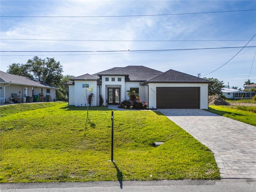 View of front facade featuring french doors, an attached garage, stucco siding, a front lawn, and decorative driveway