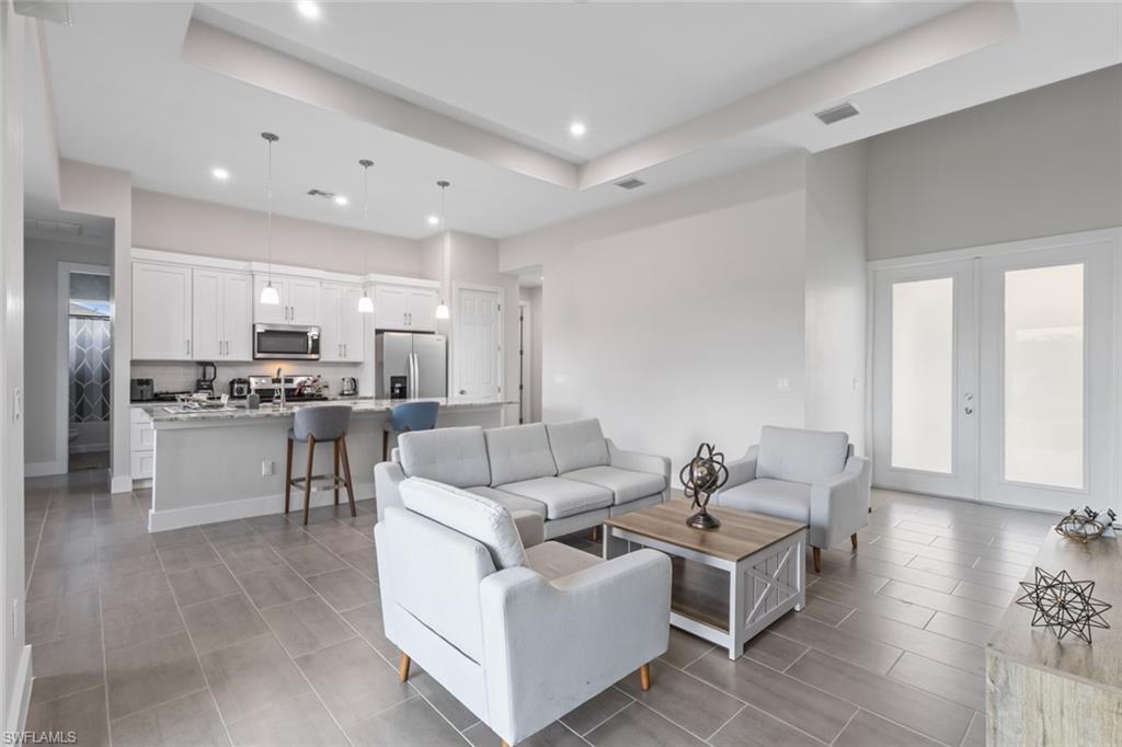 Living area featuring a raised ceiling, recessed lighting, french doors, and light tile patterned flooring