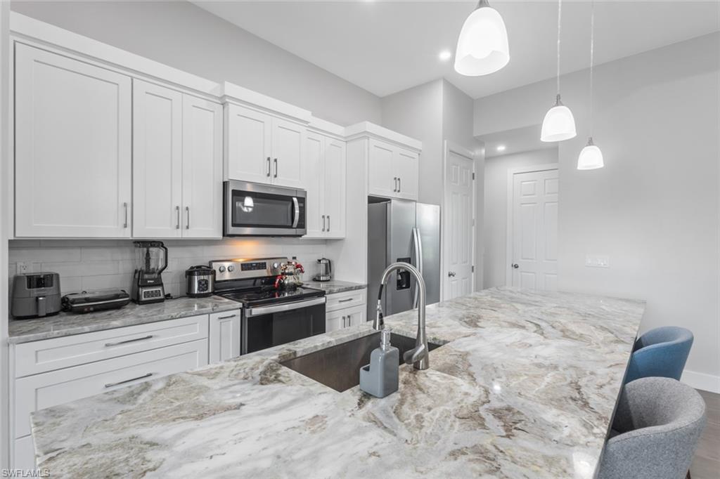 Kitchen with stainless steel appliances, white cabinets, decorative light fixtures, and recessed lighting
