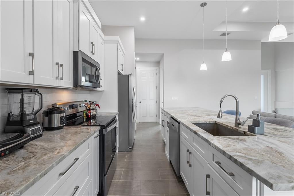 Kitchen featuring appliances with stainless steel finishes, white cabinetry, recessed lighting, decorative light fixtures, and light stone counters