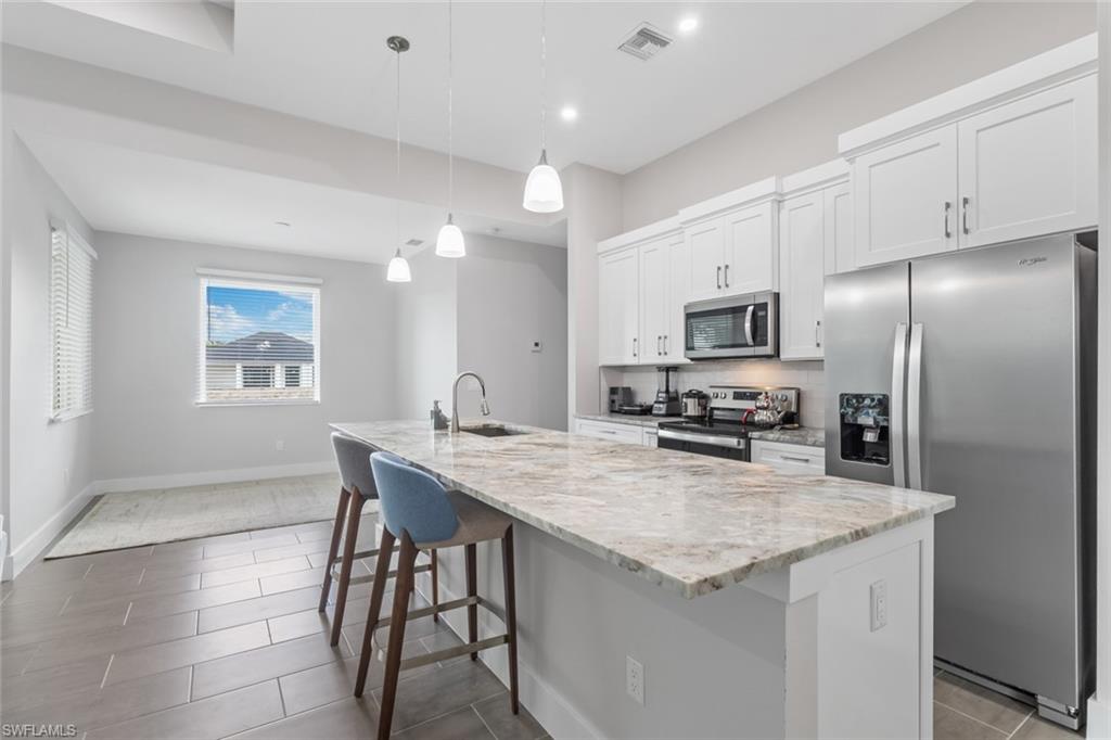 Kitchen featuring stainless steel appliances, white cabinets, a kitchen island with sink, light stone countertops, and a kitchen bar