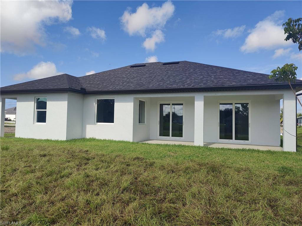 Rear view of property with stucco siding, roof with shingles, and a lawn