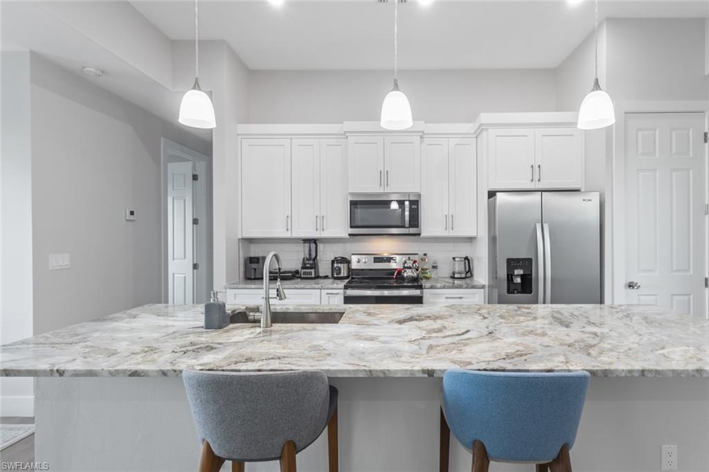 Kitchen featuring stainless steel appliances, a breakfast bar area, decorative backsplash, white cabinets, and hanging light fixtures