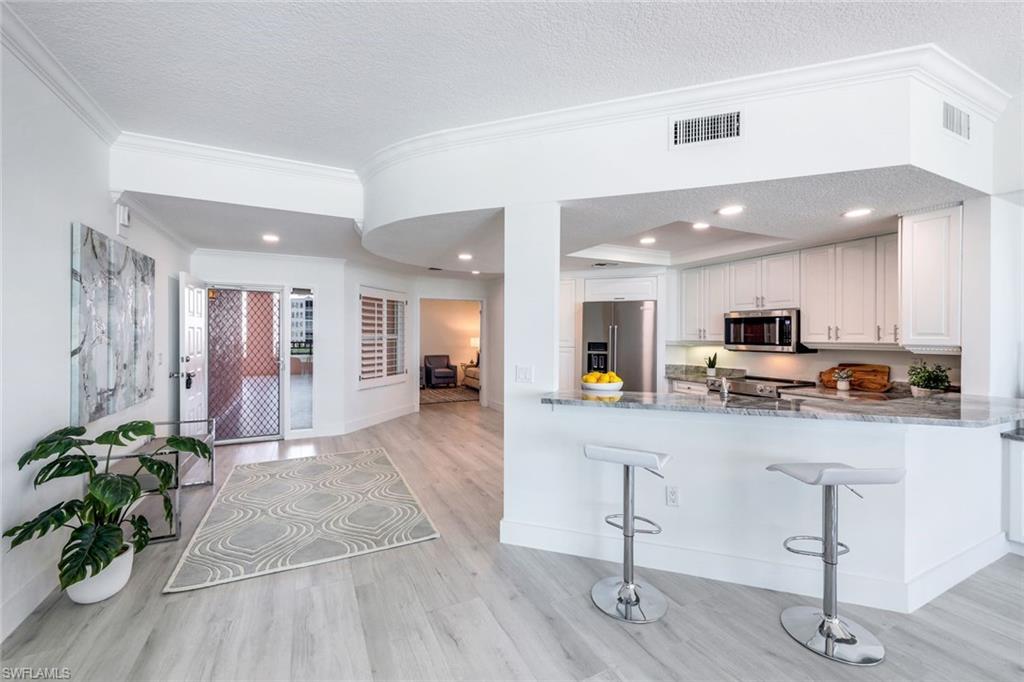 Kitchen featuring appliances with stainless steel finishes, light wood-style flooring, crown molding, a textured ceiling, and white cabinetry