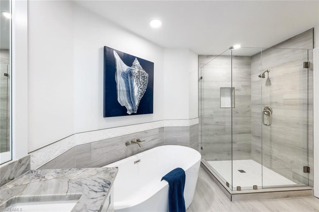Full bathroom featuring a soaking tub, a shower stall, tile walls, recessed lighting, and vanity