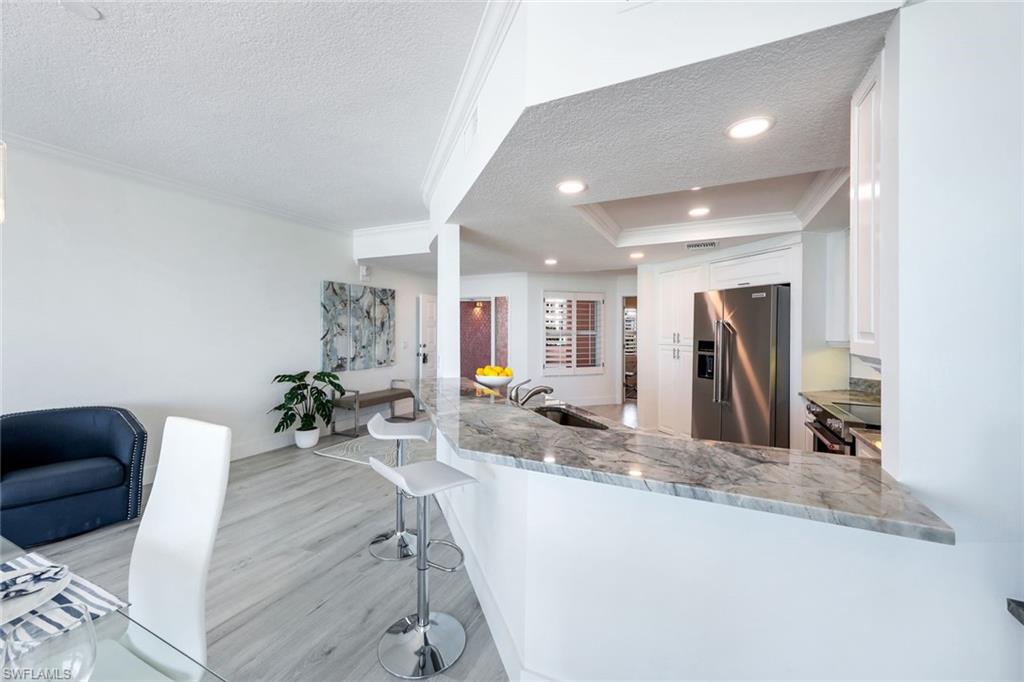 Kitchen featuring high quality fridge, a textured ceiling, a sink, ornamental molding, and light stone counters
