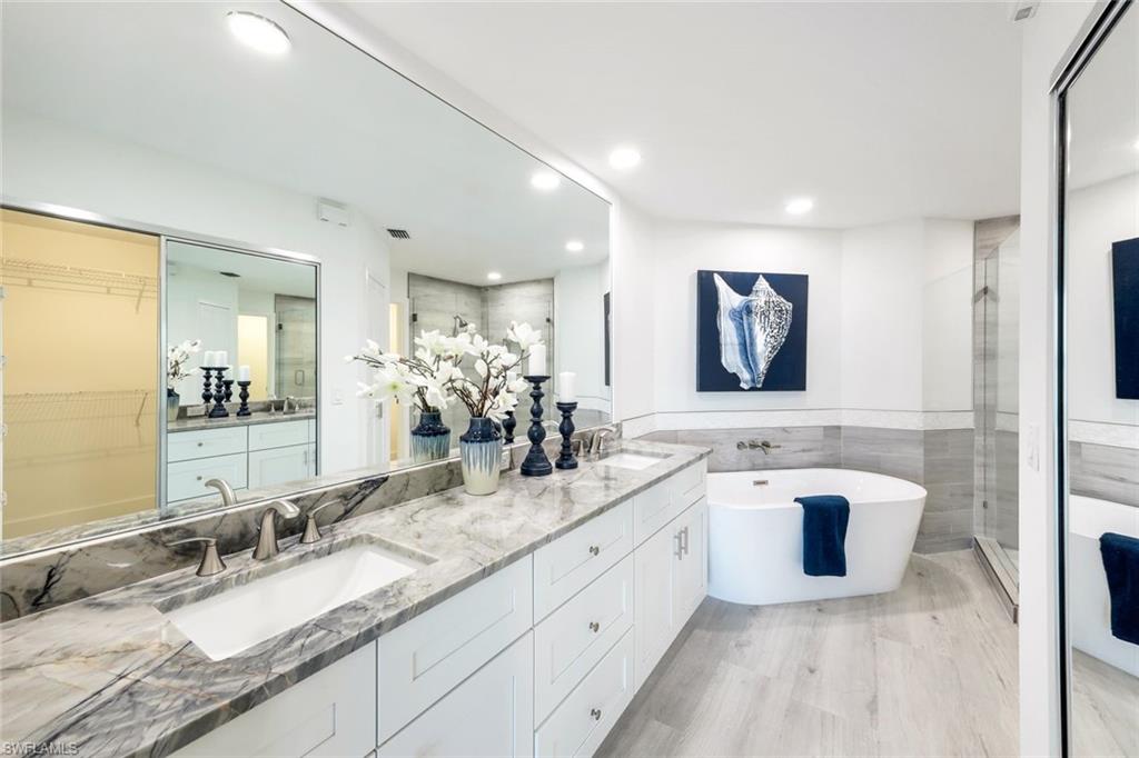Full bath featuring a shower stall, a freestanding bath, double vanity, tile walls, and recessed lighting