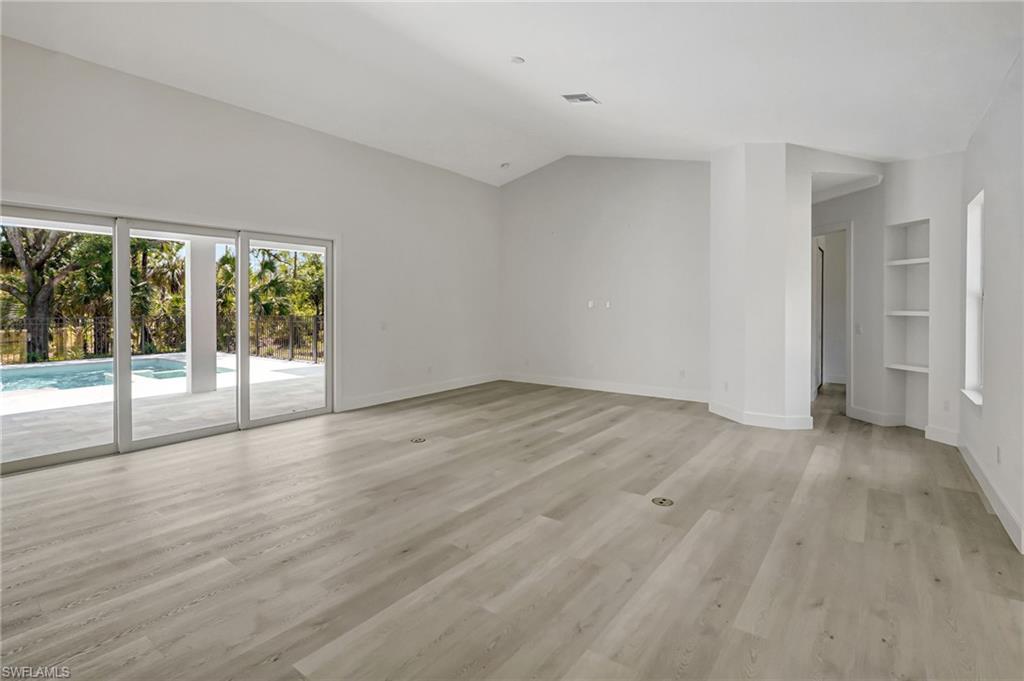 Unfurnished living room featuring light wood finished floors, baseboards, built in features, and vaulted ceiling