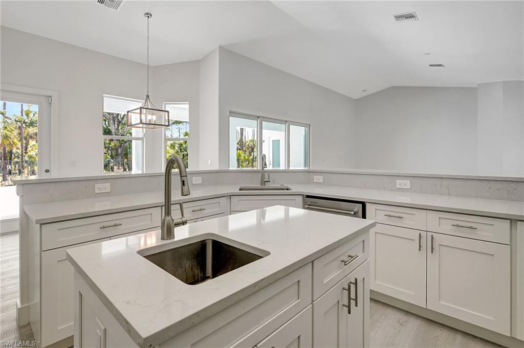Kitchen with a sink, an island with sink, white cabinets, and vaulted ceiling