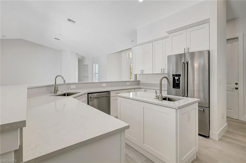 Kitchen featuring stainless steel appliances, a center island with sink, a sink, light wood-style floors, and vaulted ceiling