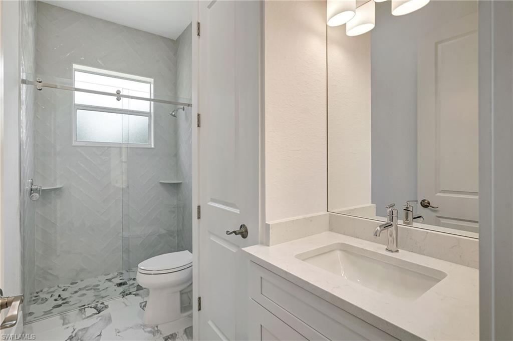 Bathroom with toilet, a stall shower, marble look tiles, and vanity