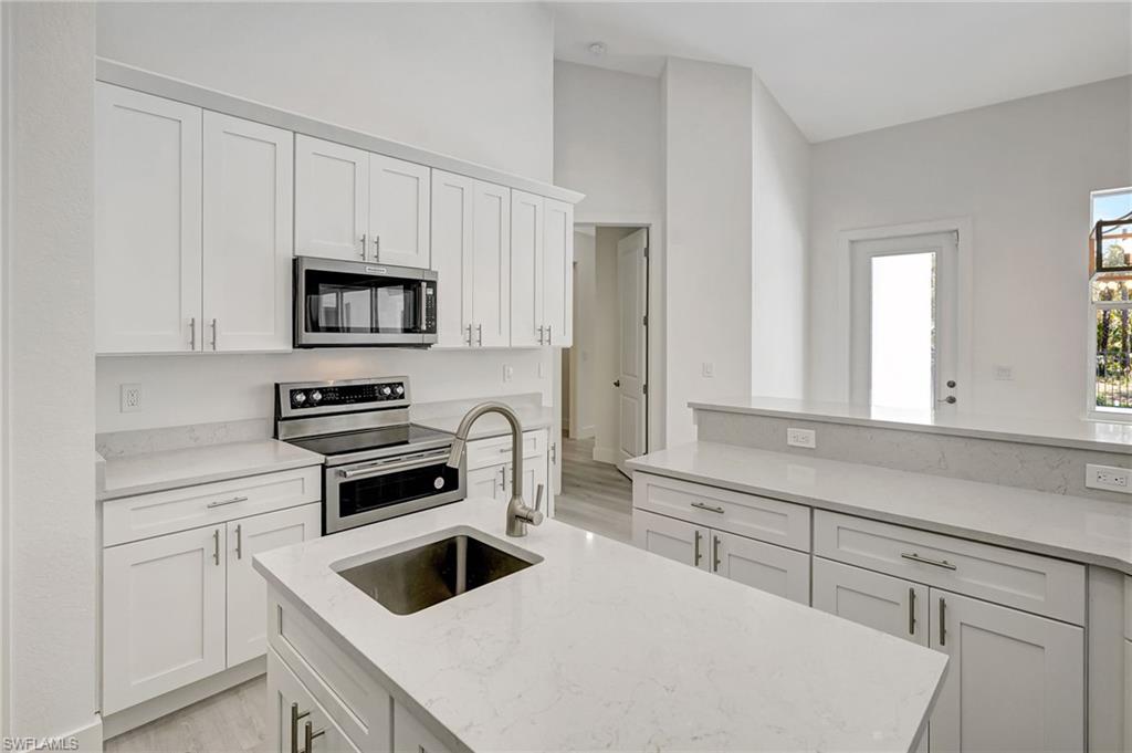 Kitchen with appliances with stainless steel finishes, a sink, light wood-type flooring, white cabinets, and light stone countertops