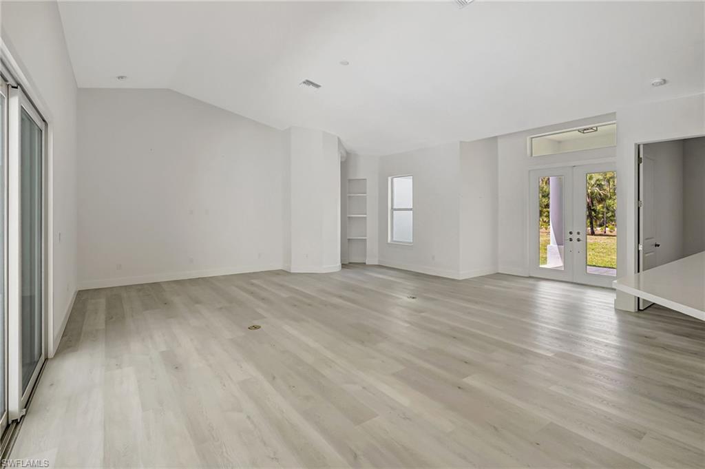 Unfurnished living room with french doors, vaulted ceiling, light wood-style floors, and baseboards