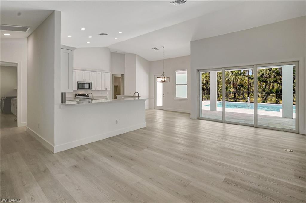 Unfurnished living room featuring high vaulted ceiling, baseboards, light wood-style flooring, and recessed lighting