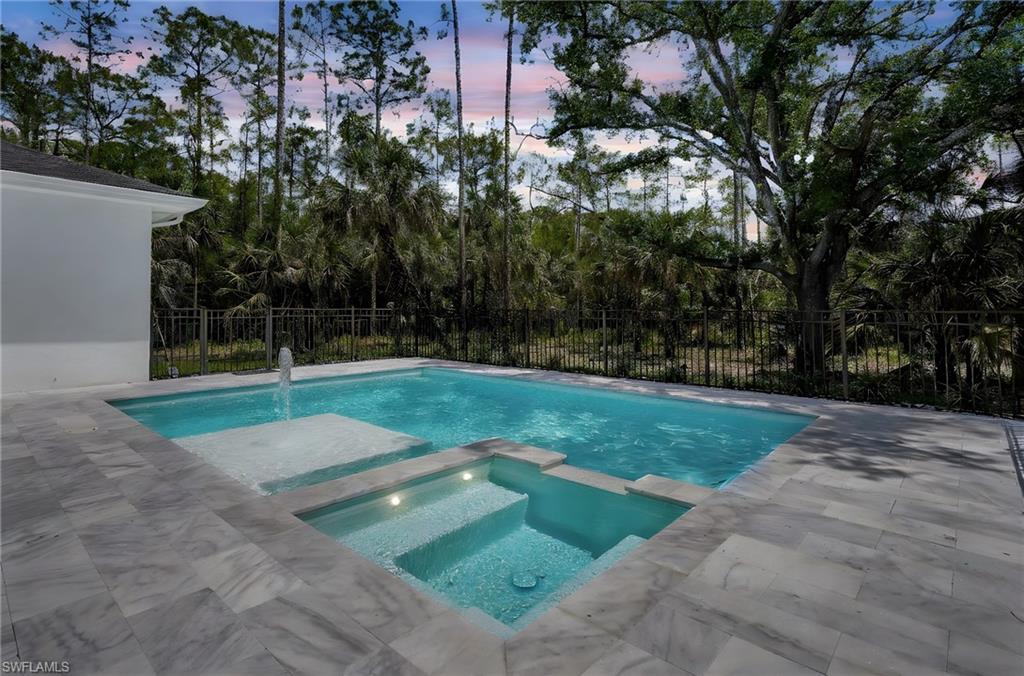 Pool at dusk featuring a pool with connected hot tub, fence, and a patio