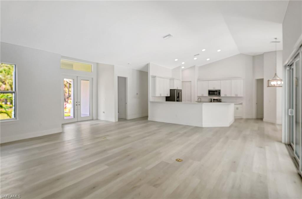 Unfurnished living room featuring high vaulted ceiling, light wood-type flooring, baseboards, and recessed lighting