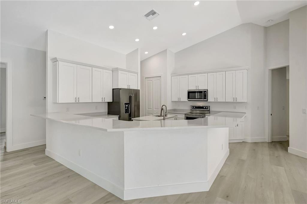Kitchen featuring stainless steel appliances, baseboards, high vaulted ceiling, white cabinetry, and light wood-style floors