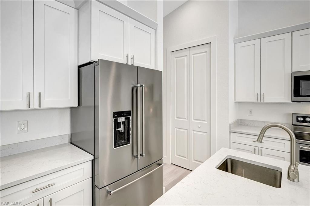 Kitchen featuring stainless steel appliances, a sink, white cabinetry, and light stone counters