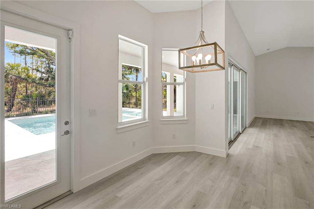 Unfurnished dining area featuring a chandelier, light wood-style flooring, lofted ceiling, and baseboards