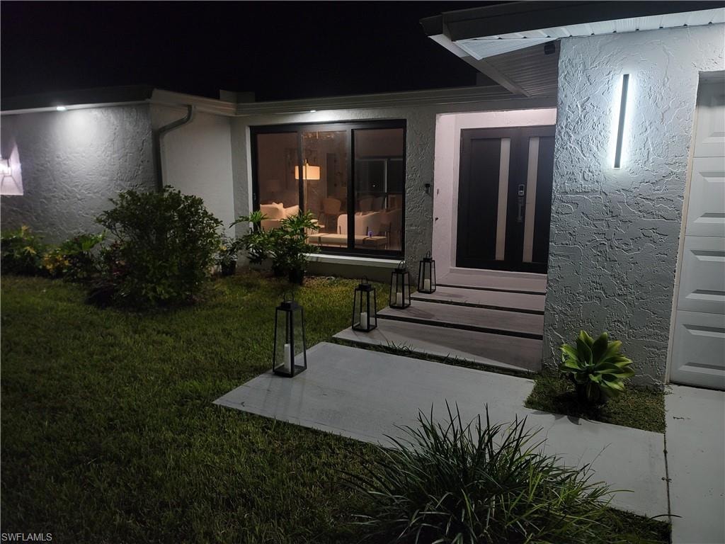 Exterior entry at twilight with a yard and stucco siding