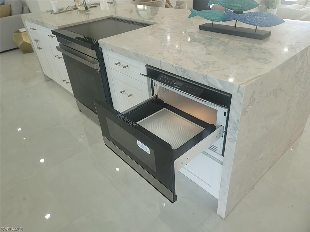 Kitchen with a warming drawer, light stone countertops, range with electric stovetop, white cabinetry, and light tile patterned floors