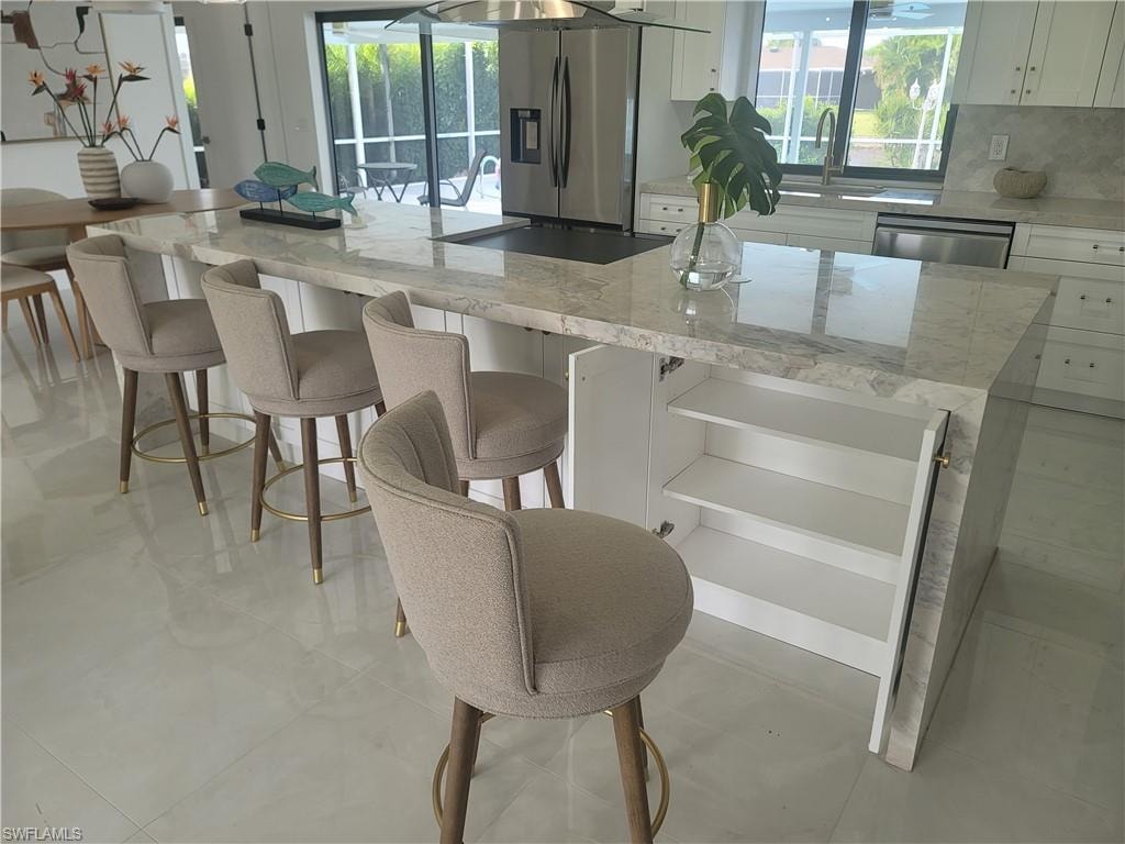 Kitchen with light stone countertops, white cabinetry, a kitchen island, and a kitchen bar