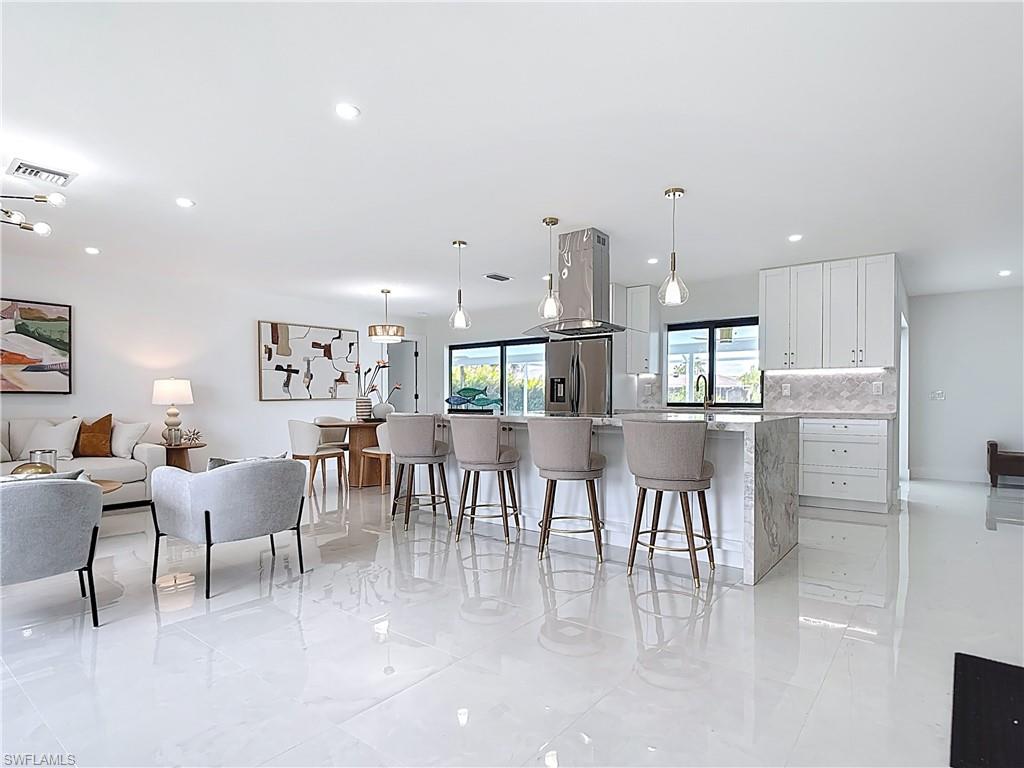 Kitchen with stainless steel fridge, a breakfast bar area, white cabinets, decorative backsplash, and hanging light fixtures