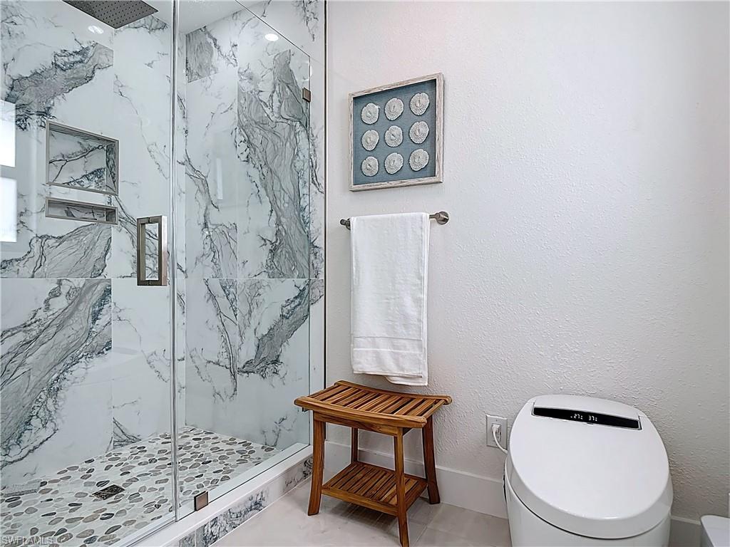 Full bath with a marble finish shower and toilet