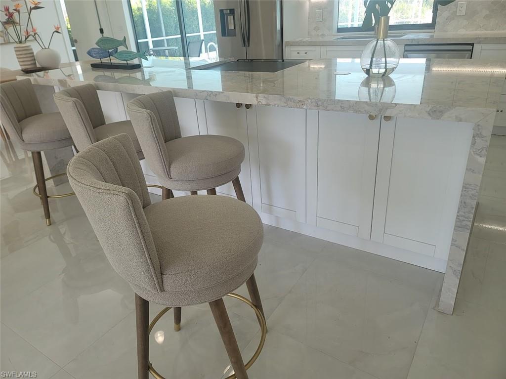 Kitchen featuring white cabinetry, light stone counters, stainless steel fridge with ice dispenser, and a kitchen bar