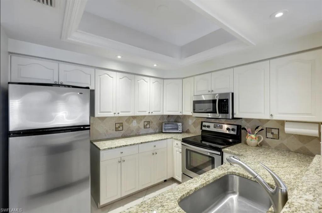 Kitchen with appliances with stainless steel finishes, a sink, light stone counters, white cabinets, and recessed lighting