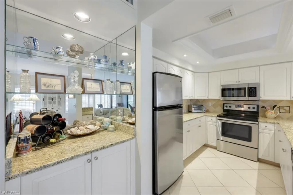 Kitchen featuring stainless steel appliances, decorative backsplash, white cabinets, light stone counters, and recessed lighting