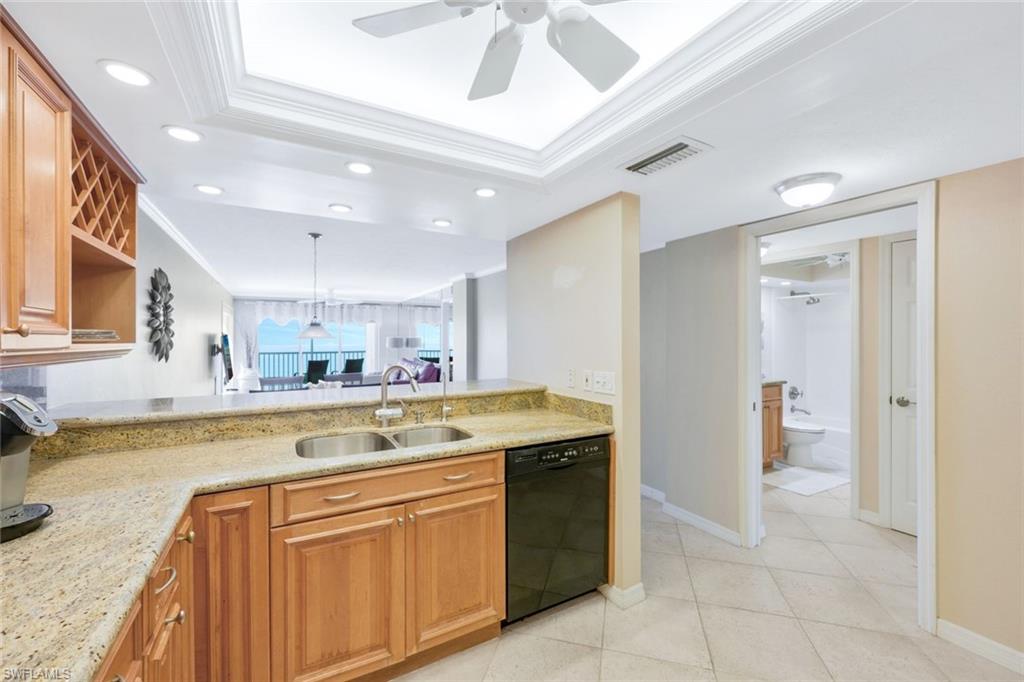 Kitchen with ceiling fan, crown molding, light stone counters, black dishwasher, and sink