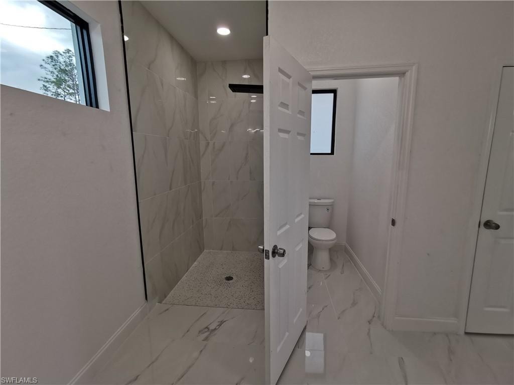 Full bath featuring a marble finish shower and light marble finish flooring