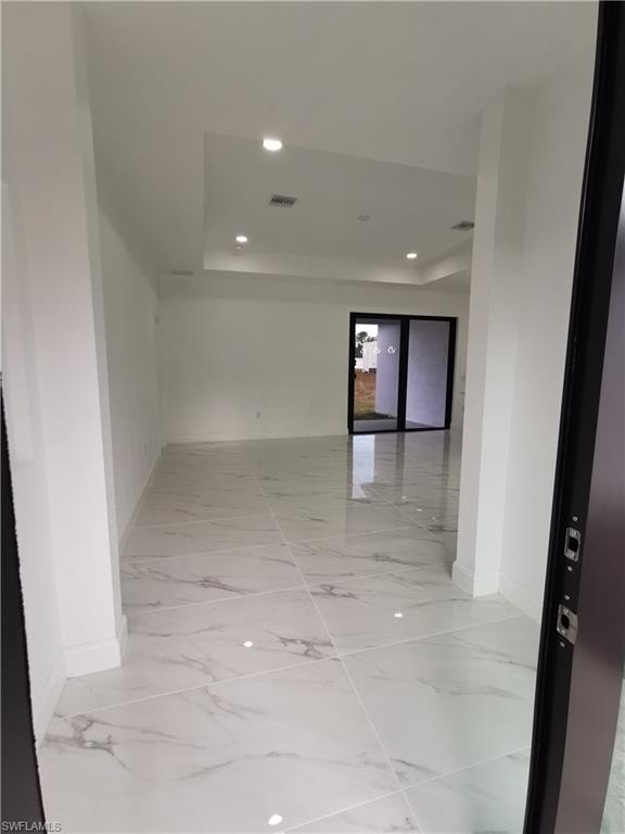 Corridor with light marble finish floors, recessed lighting, and a tray ceiling