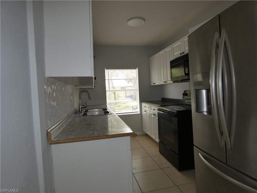 Kitchen featuring black appliances, a sink, white cabinetry, light tile patterned floors, and backsplash